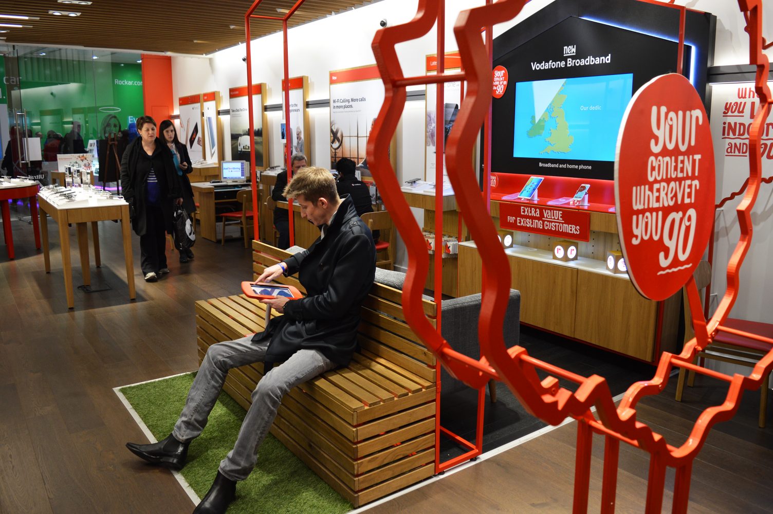 Customer sitting down on bench and using ipad. Vodafone Quad Play, Retail Store and Service Design by Household.